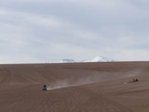Flache trockene Wüste und im Hintergrund schneebedeckte Gipfel